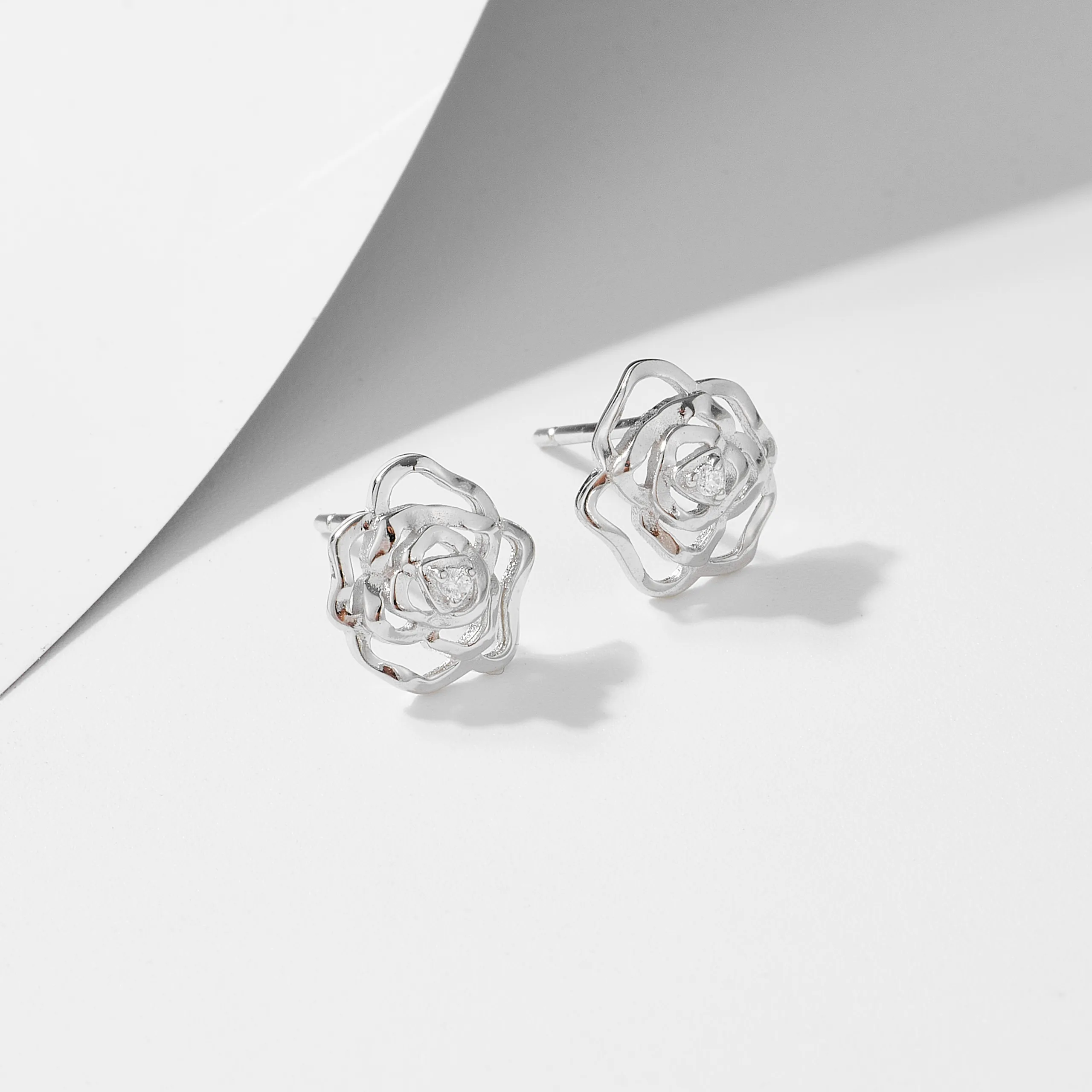 Sterling silver rose-shaped stud earrings with delicate cubic zirconia, minimalist floral jewelry design.
