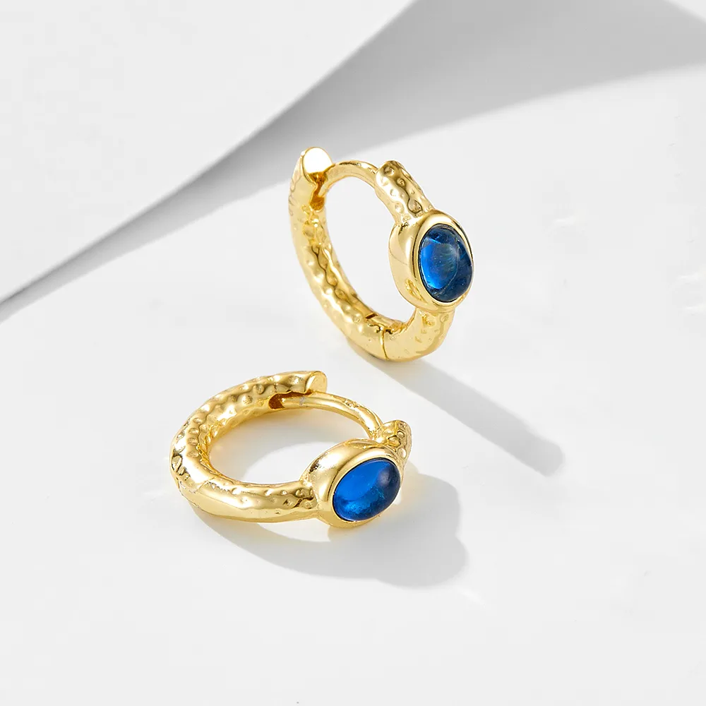 Gold hoop earrings with blue gemstone cabochon, textured design for an elegant and artistic look.