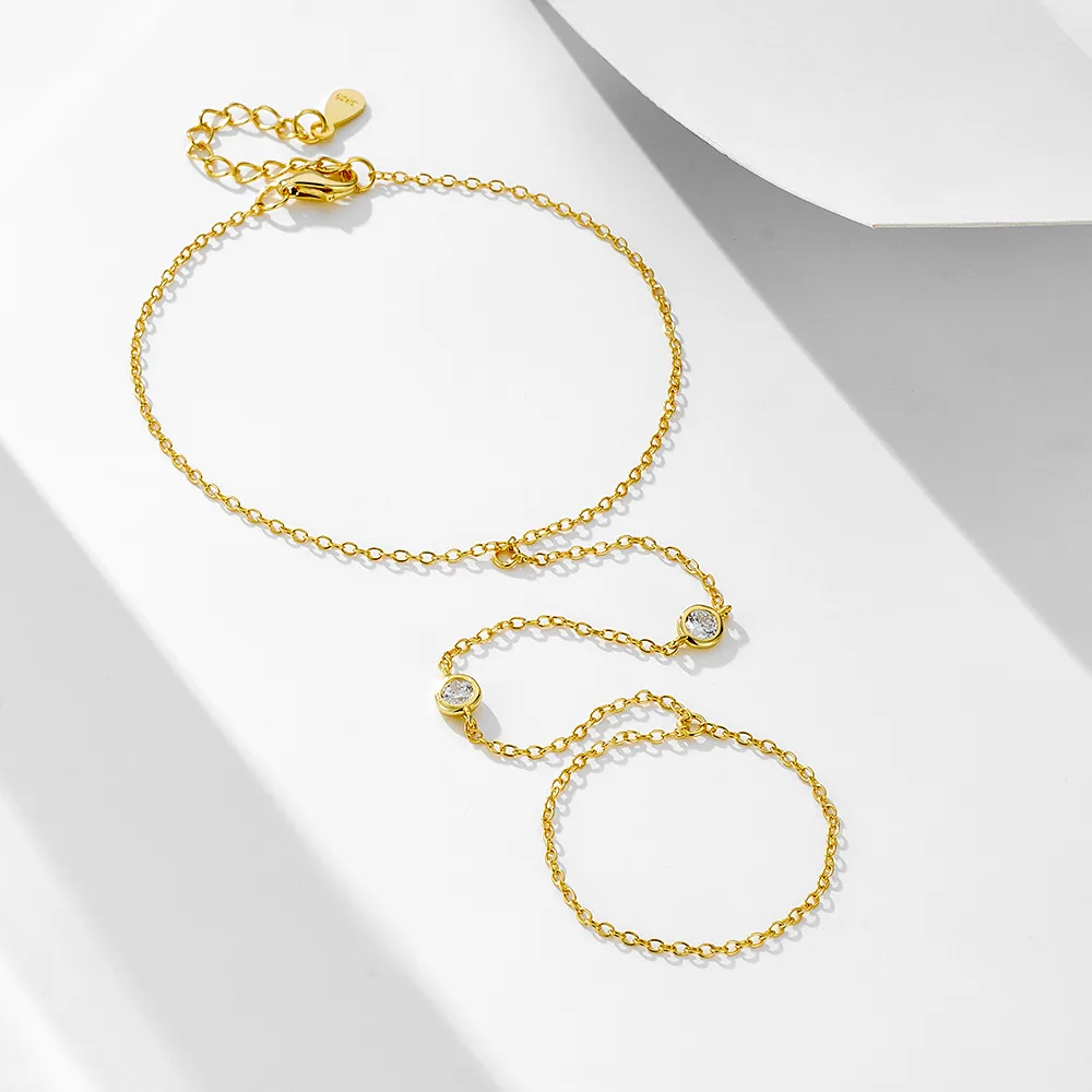 Delicate gold hand chain bracelet with cubic zirconia accents, modern jewelry design connecting wrist and finger.